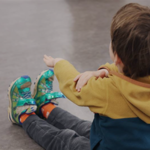 Child sitting on the group, legs out straight and reaches for their legs in a stretch.