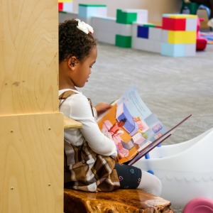 Young library patron sitting on a bench and reading a picture book