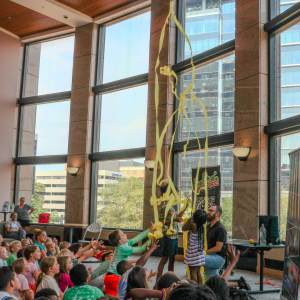 Mr. Science does an experiment with yellow streamers in the air. Children ages 7-11 watch with outstretched arms