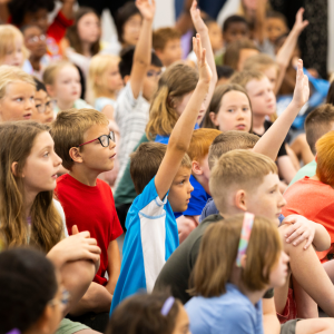 Children raise their hands to be called on during a free Summer at the Library educational event.