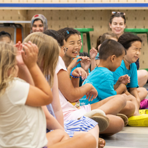 Many school-aged children sit on the floor laughing during a free summer library event