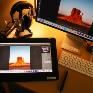 Headphones, computer, and tablet on a workstation table with the image of desert mountains