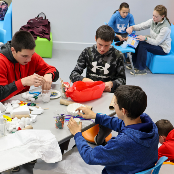 Three young boys sit around a table making a project