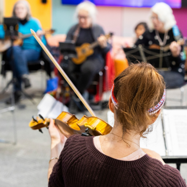 Violinist plays music alongside other musicians with instruments at the library