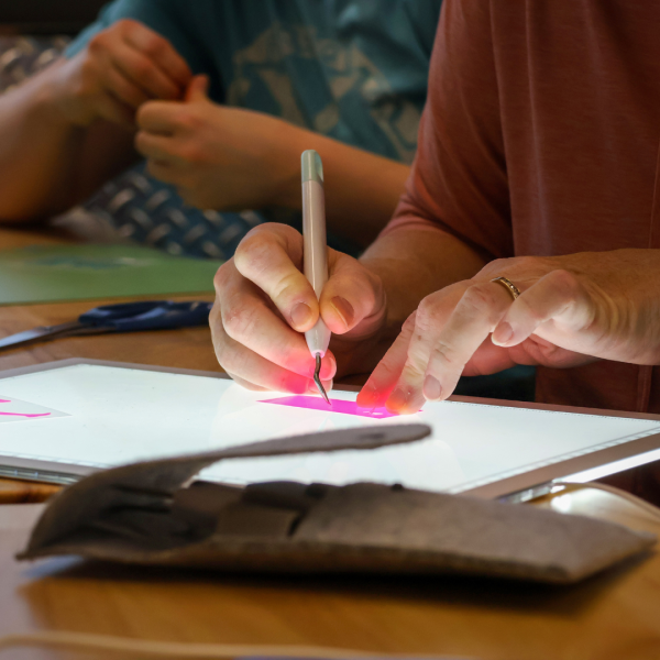 Hands using a pick tool on a project, illuminated by the glow of an iPad screen