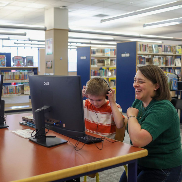 Child and caregiver use a computer together at the library.