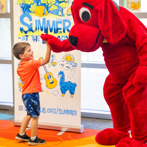 Young patron high fives Clifford the red dog at one of the Summer at the Library kickoff party