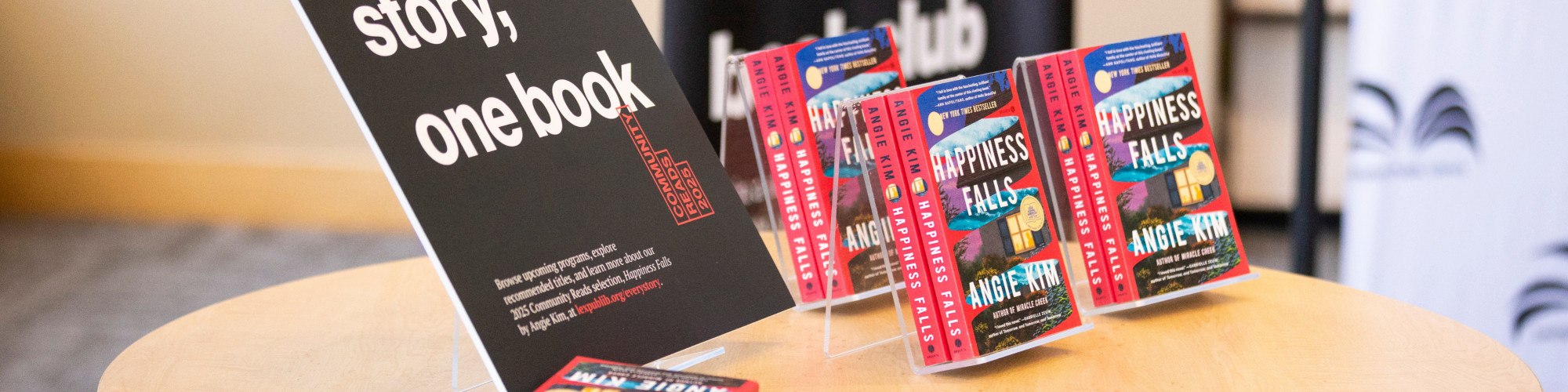2025 Community Reads book "Happiness Falls" by Angie Kim sits on a circle table.
