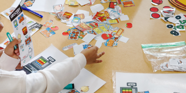 Child and caregiver sitting together at a table covered with papers and activities during a kindergarten readiness program.