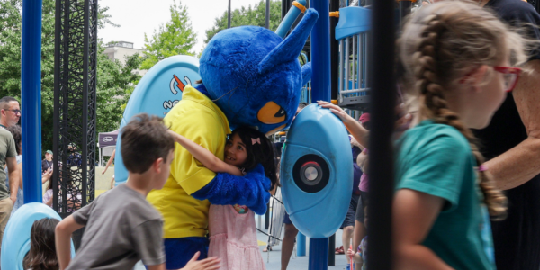 Child hugs Pete the Cat character while children play in Phoenix Park outside of Central Library